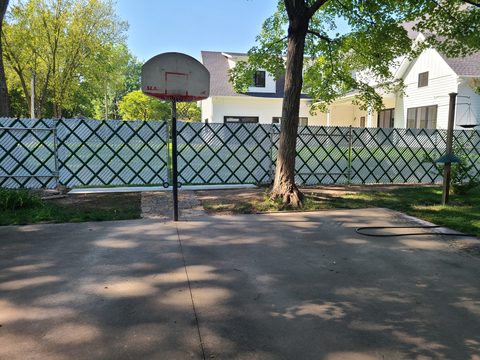 Chain link fence with white privacy slats around a backyard basketball court in Northwest Arkansas