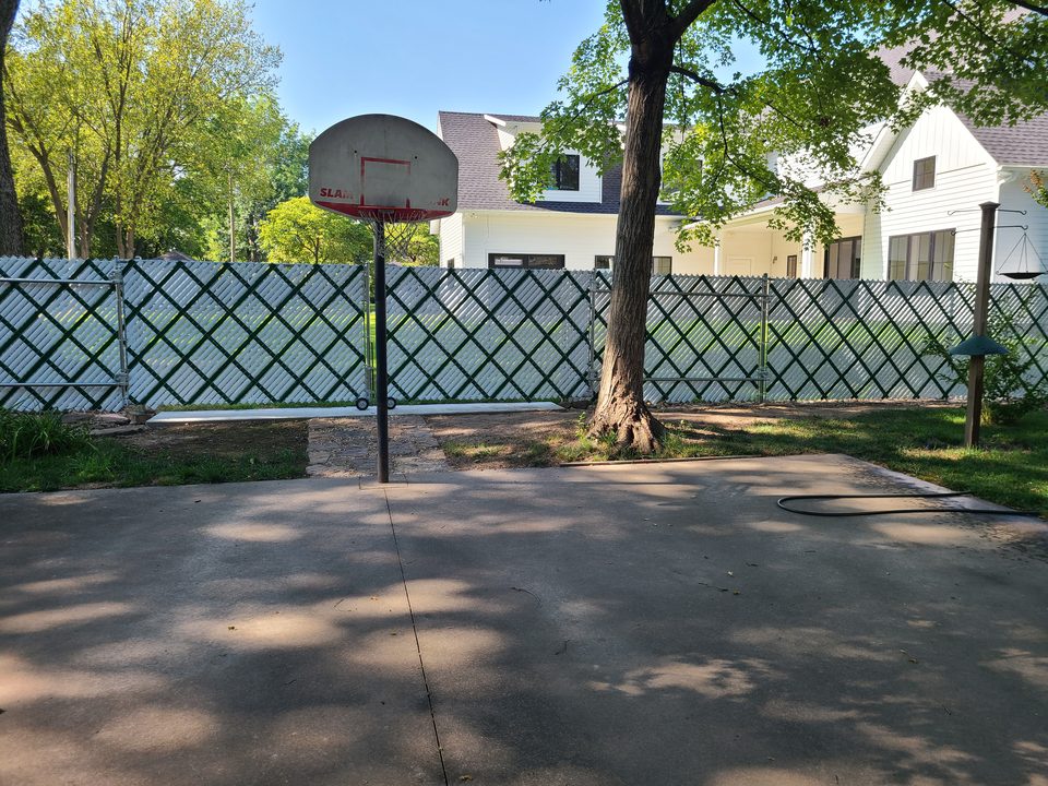Privacy-slatted chain-link fence around a residential basketball court in Northwest Arkansas
