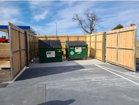 Cedar-and-steel dumpster enclosure with swing gates at a commercial site in Northwest Arkansas