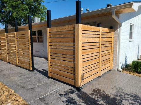 Modern horizontal-slat wood privacy screens with steel posts beside a home in Northwest Arkansas