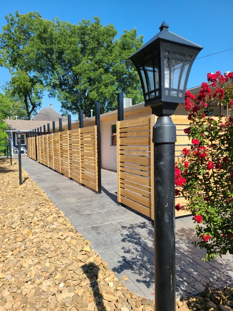 Modern horizontal cedar-slat fence with a black lamp post on a paver walkway in Northwest Arkansas