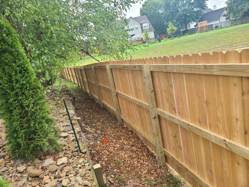 Cedar privacy fence following a downhill grade beside a rock drainage bed in Northwest Arkansas