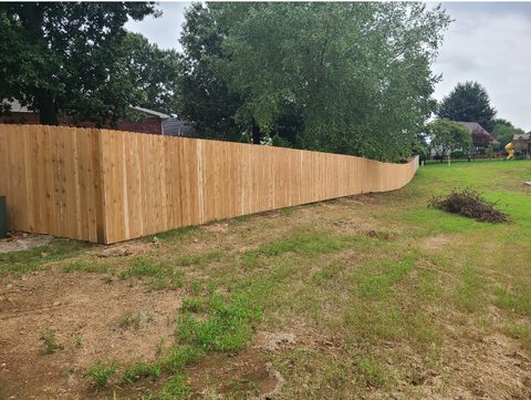 Long cedar privacy fence stepping down a grassy grade past mature trees in Northwest Arkansas