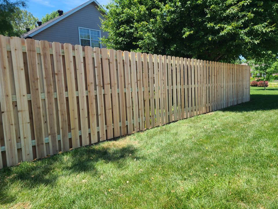 Shadowbox-style wood privacy fence running along a mowed lawn beside a house and mature trees in Northwest Arkansas